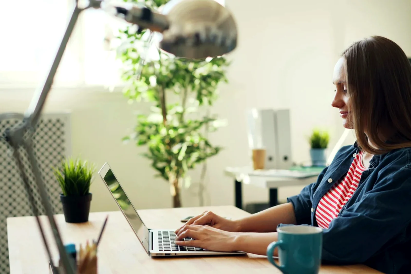 Freelancer working at a bright desk with a laptop, coffee, and daylight in the room.
