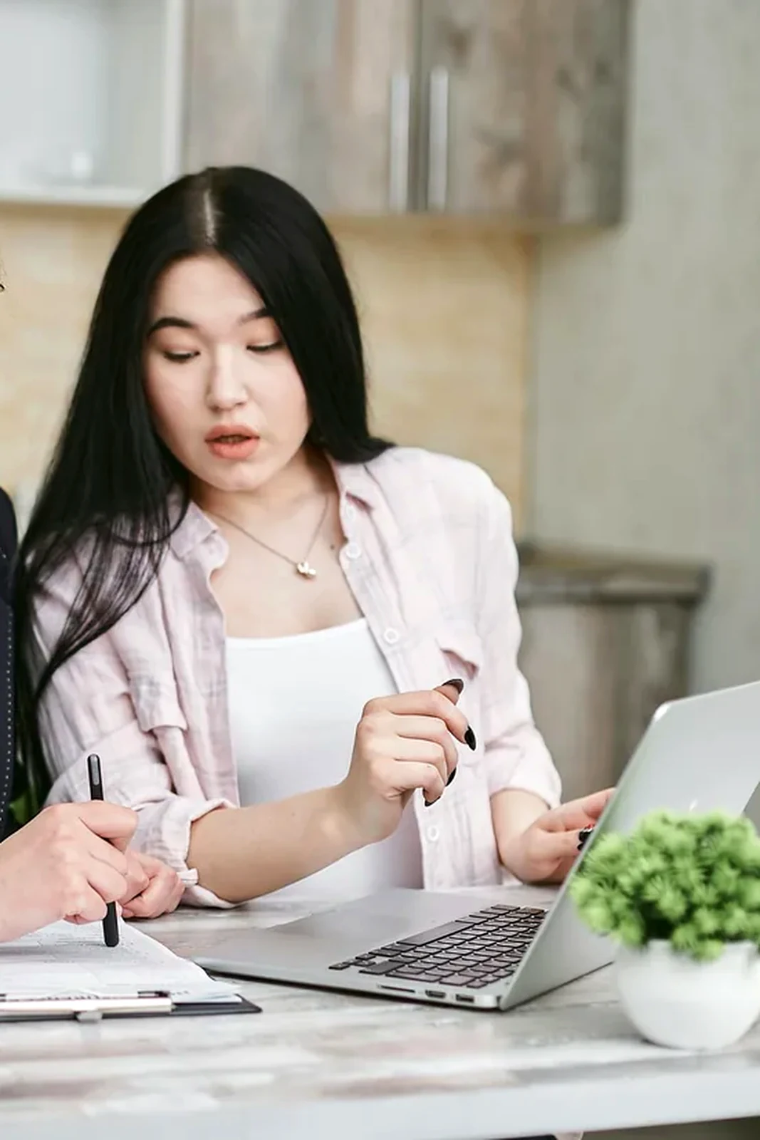 Two professionals reviewing a laptop and written notes together at a clean table.